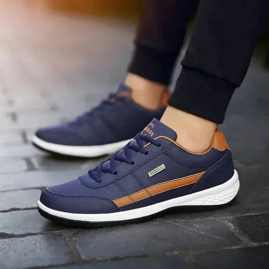 Scarpe da ginnastica blu e marroni su pavimento in pietra, design moderno, suola bianca, adatte per sport e tempo libero.