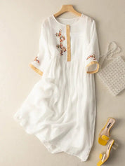 Abito bianco in chiffon con ricami floreali, maniche a tre quarti, abbinato a borsa di perle e sandali gialli. Elegante e femminile.