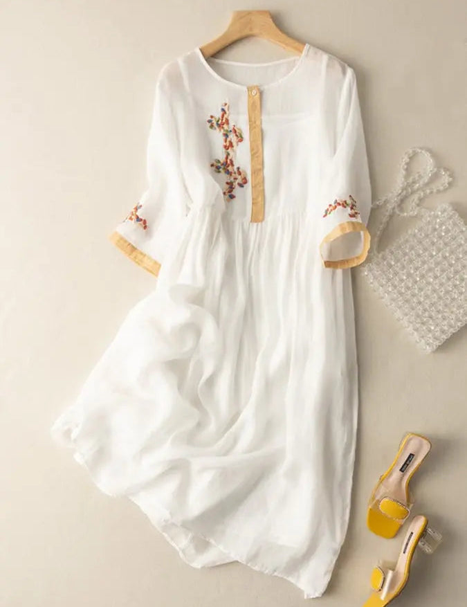 Abito bianco in chiffon con ricami floreali, maniche a tre quarti, abbinato a borsa di perle e sandali gialli. Elegante e femminile.