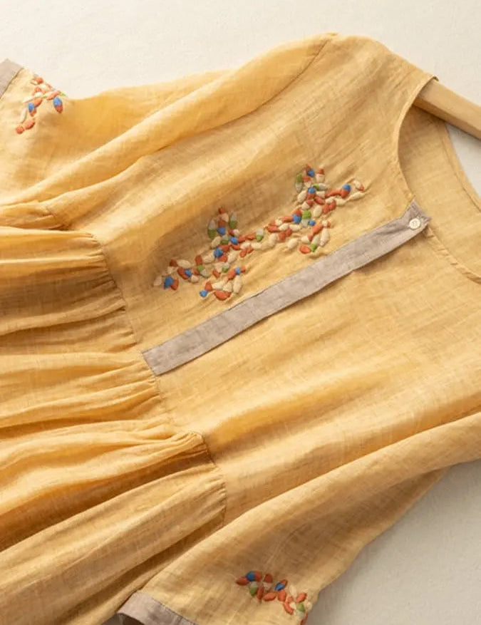 Abito giallo in lino con ricami colorati, maniche corte e scollo rotondo. Design elegante e casual, perfetto per la moda estiva femminile.
