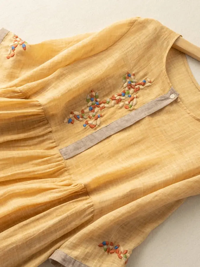 Abito giallo in lino con ricami colorati, maniche corte e scollo rotondo. Design elegante e casual, perfetto per la moda estiva femminile.