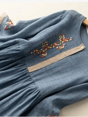 Abito blu in lino con ricami floreali colorati, maniche lunghe, scollo rotondo e chiusura frontale a bottoni. Elegante e casual.