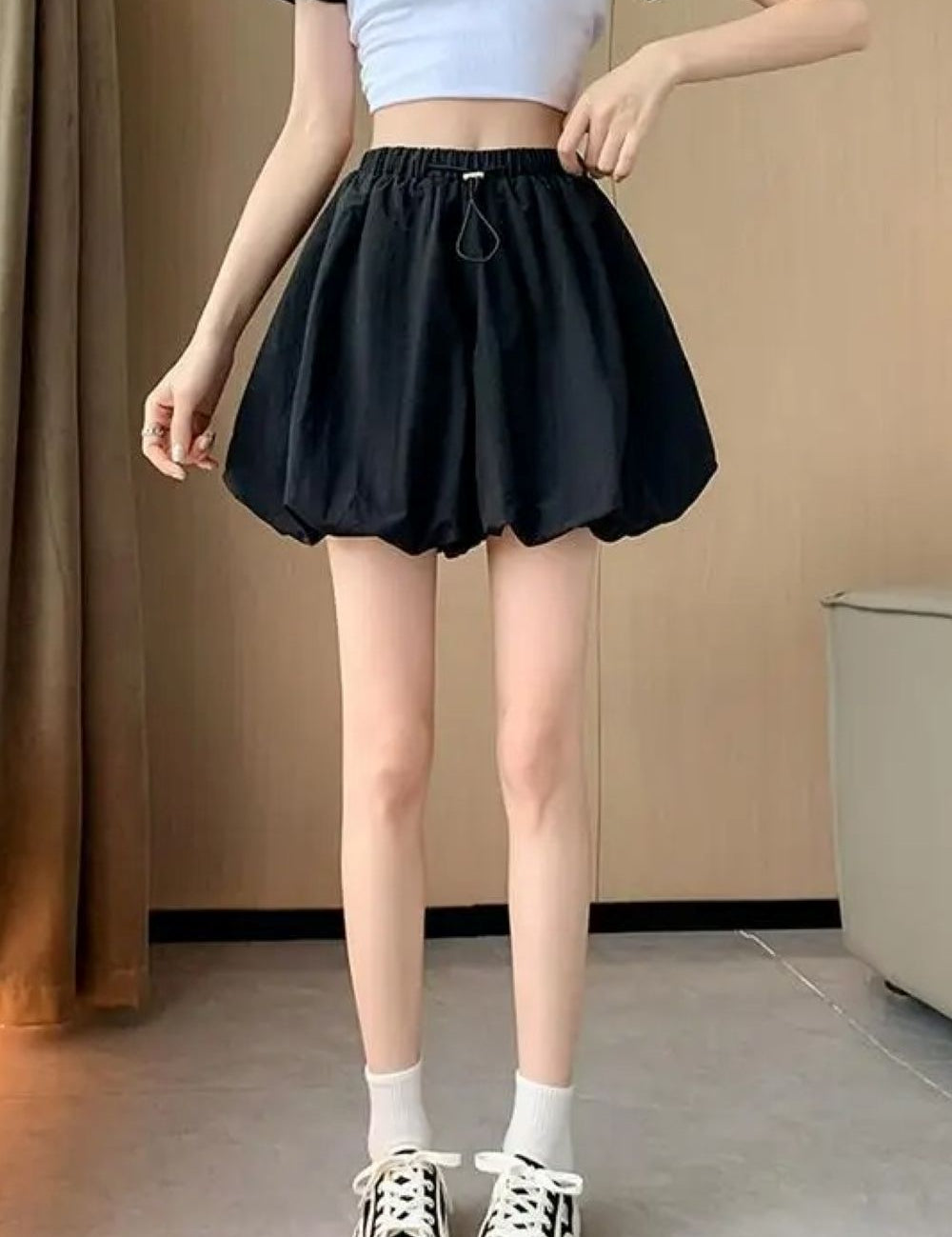 Donna in top bianco e gonna nera a palloncino, scarpe da ginnastica bianche e nere. Moda casual estiva, abbigliamento femminile trendy.