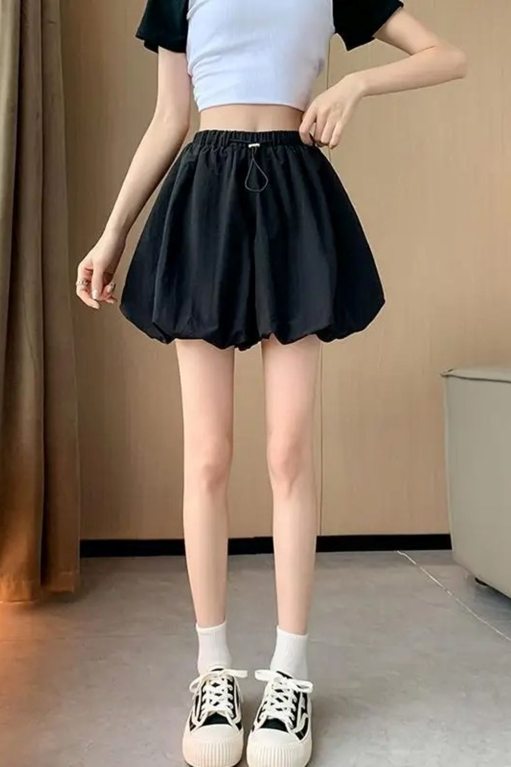 Donna in top bianco e gonna nera a palloncino, scarpe da ginnastica bianche e nere. Moda casual estiva, abbigliamento femminile trendy.