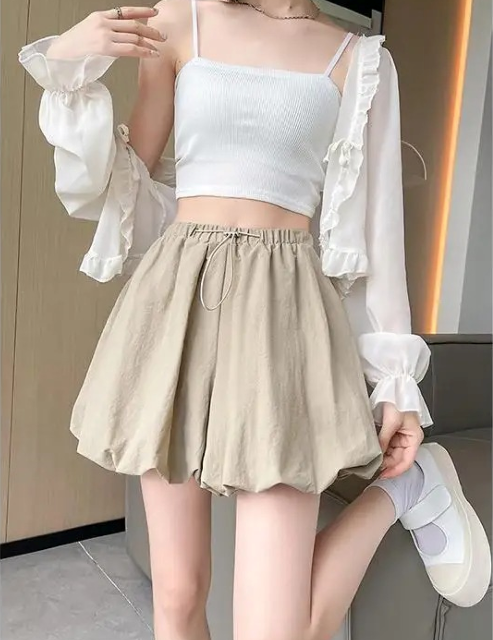Donna con top bianco e pantaloncini beige, posa moderna. Moda estiva casual, abbigliamento femminile trendy, outfit leggero e confortevole.