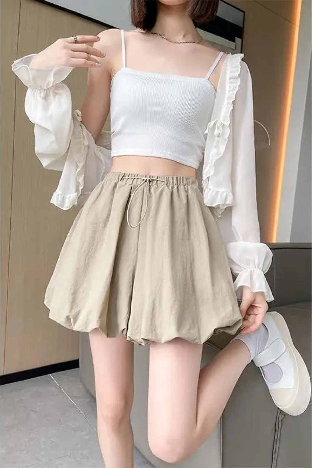 Donna con top bianco e pantaloncini beige, posa moderna. Moda estiva casual, abbigliamento femminile trendy, outfit leggero e confortevole.