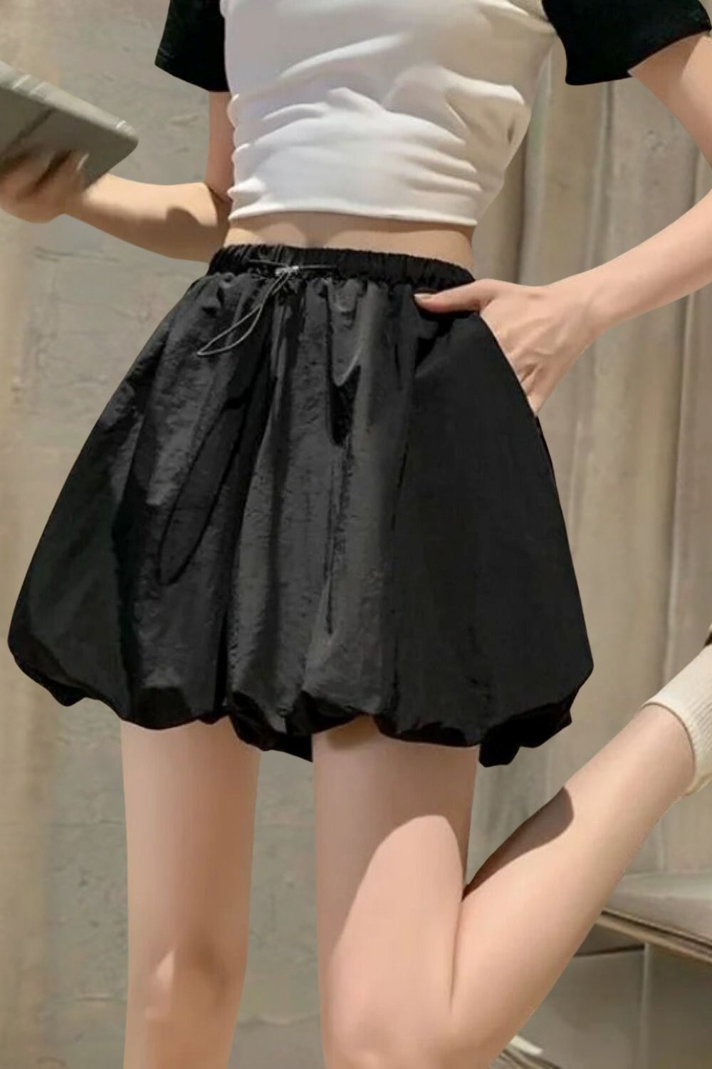 Gonna nera a palloncino, vita alta, con tasche, indossata da una donna. Moda estiva casual, tessuto leggero, abbinata a top bianco e calzini.