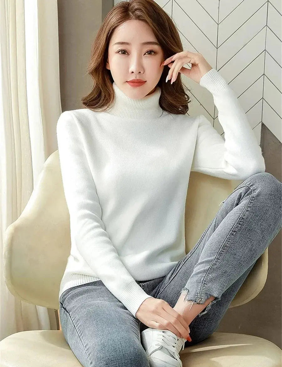 Donna seduta indossa maglione bianco a collo alto e jeans grigi. Moda autunnale, abbigliamento casual elegante, stile minimalista.