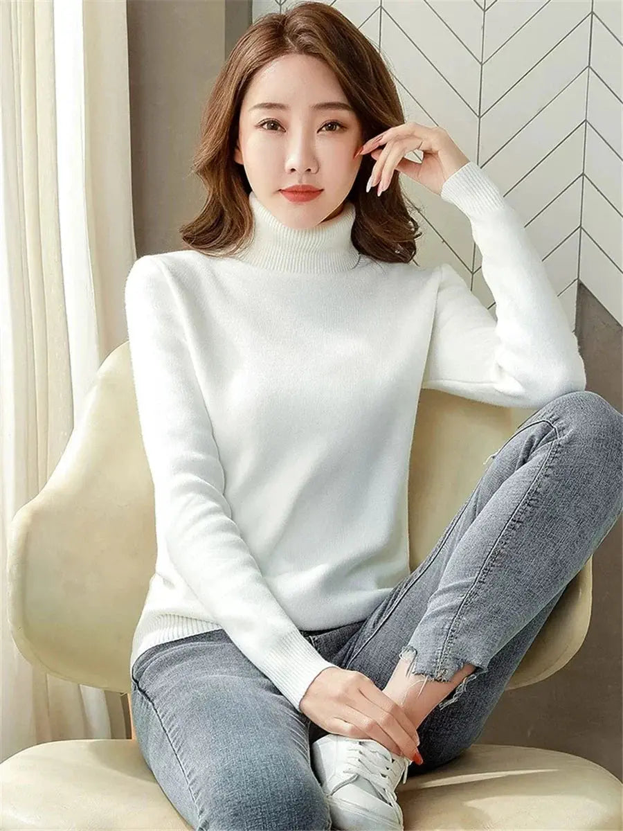 Donna seduta indossa maglione bianco a collo alto e jeans grigi. Moda autunnale, abbigliamento casual elegante, stile minimalista.