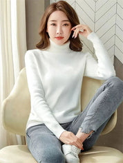 Donna seduta indossa maglione bianco a collo alto e jeans grigi. Moda autunnale, abbigliamento casual elegante, stile minimalista.