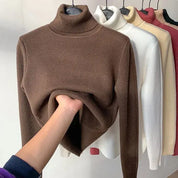 Maglioni a collo alto in vari colori su appendiabiti, con mano che tocca il maglione marrone. Tessuto morbido, moda autunno inverno, abbigliamento casual.
