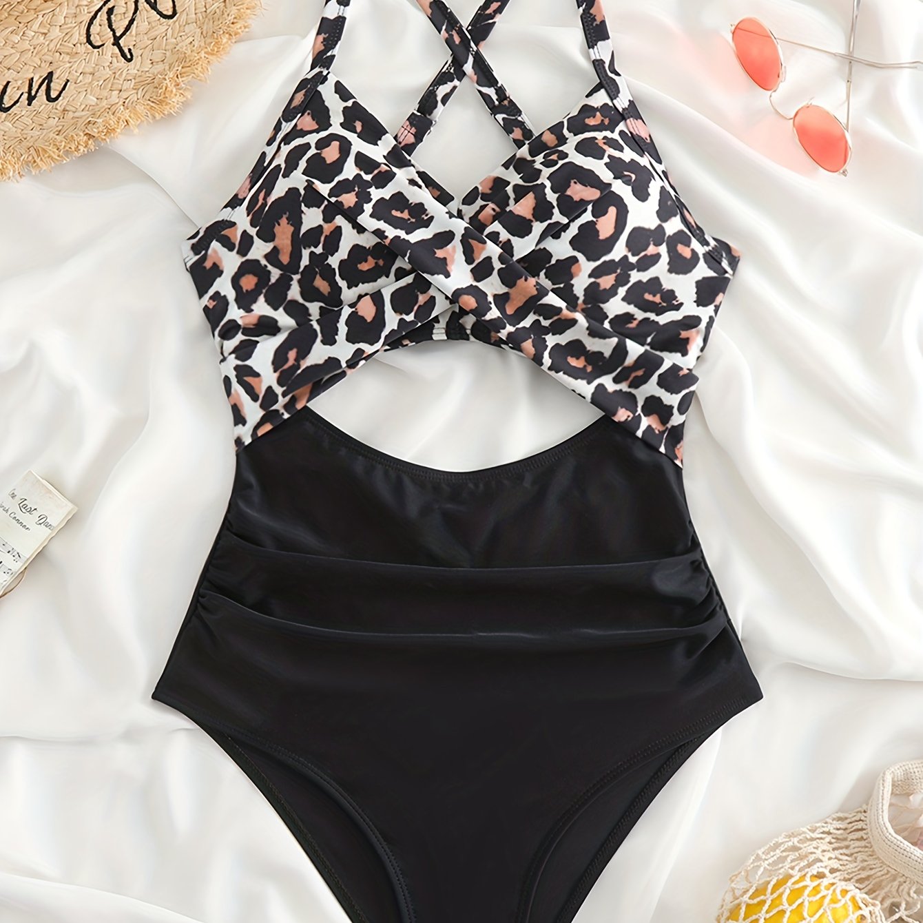 Costume intero donna leopardato e nero, design incrociato, su sfondo bianco con accessori estivi. Moda mare, abbigliamento da spiaggia elegante.
