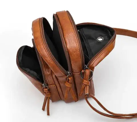 Zaino in pelle marrone con tre scomparti, cerniere robuste e tracolla regolabile. Design elegante e funzionale per moda e praticità quotidiana.