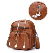 Zaino in pelle marrone con tasche multiple e foro per auricolari. Design elegante e pratico, ideale per viaggi e uso quotidiano.