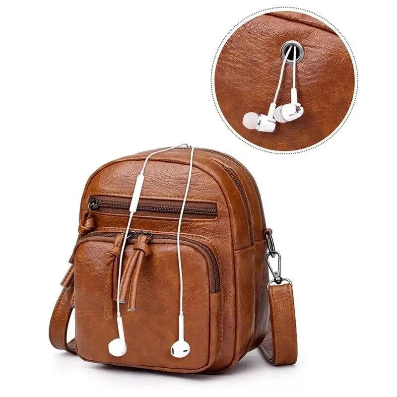 Zaino in pelle marrone con tasche multiple e foro per auricolari. Design elegante e pratico, ideale per viaggi e uso quotidiano.