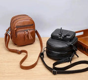 Due borse a tracolla in pelle, una marrone e una nera, su un tavolo di legno. Design compatto, tasche multiple, ideale per uomo e donna.