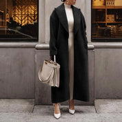 Cappotto lungo nero elegante donna, abbinato a borsa beige e scarpe bianche, moda autunno inverno, look sofisticato urbano.