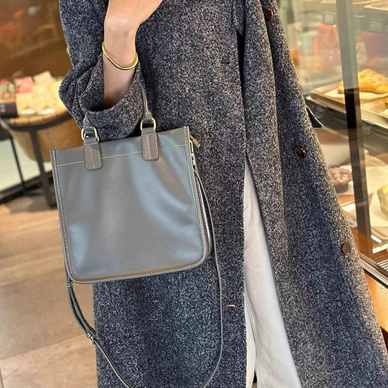 Borsa a tracolla grigia in pelle, indossata da una persona con cappotto grigio. Accessorio moda elegante, perfetto per l'autunno e l'inverno.