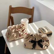 Due borse in tessuto beige con fiocchi, una con motivi a ciliegia rossa e l'altra a pois neri, su tavolo bianco accanto a sedia e bevanda.