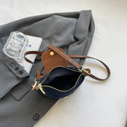 Borsa a tracolla in pelle marrone su giacca grigia, con libro e bicchiere di vetro. Design elegante, accessori moda, stile casual chic.