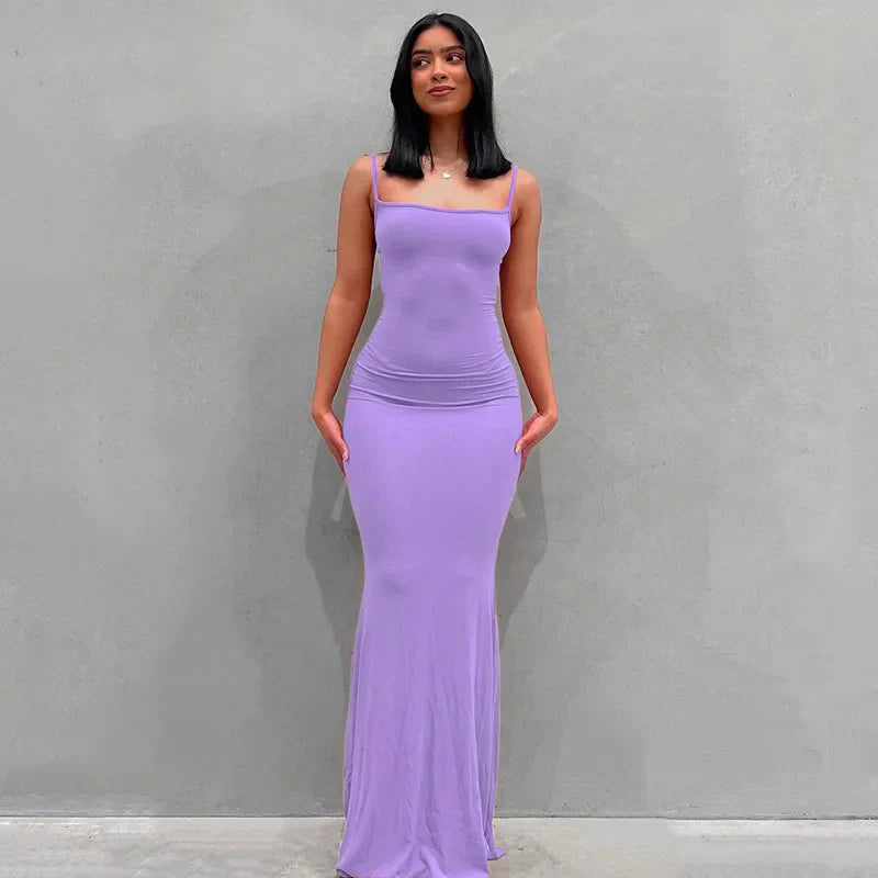 Abito lungo aderente viola, senza maniche, con scollo quadrato, indossato da una donna su sfondo grigio. Elegante e moderno, perfetto per eventi serali.