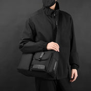 Uomo con giacca nera indossa borsa a tracolla nera elegante, multifunzionale, con tasche, ideale per lavoro e viaggio. Accessorio moda maschile.