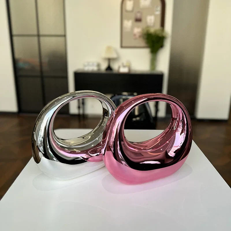 Due sculture astratte in metallo lucido, una argento e una rosa, su piedistallo bianco in un ambiente moderno. Arte contemporanea, design elegante.