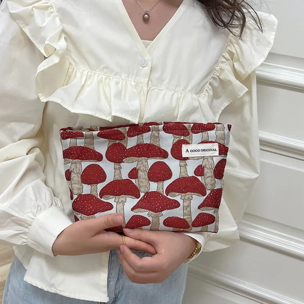 Donna con camicetta bianca tiene una pochette con stampa di funghi rossi. Accessorio moda originale, design unico, perfetto per look autunnali.