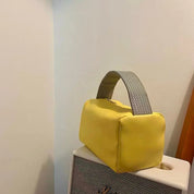 Borsa a mano gialla su amplificatore, design moderno, manico grigio intrecciato, accessorio moda elegante, stile contemporaneo.
