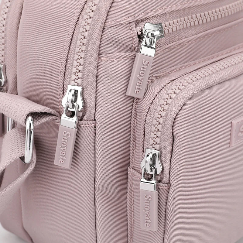 Zaino rosa in tessuto resistente con cerniere multiple e dettagli in metallo argentato, ideale per moda femminile e viaggi.