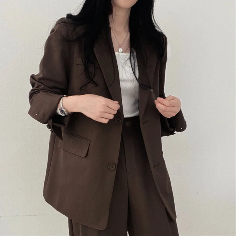 Donna in blazer marrone elegante, abbinato a pantaloni coordinati e top bianco. Moda femminile, abbigliamento formale, stile business casual.