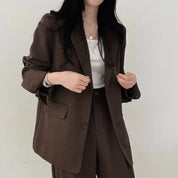 Donna in blazer marrone elegante, abbinato a pantaloni coordinati e top bianco. Moda femminile, abbigliamento formale, stile business casual.