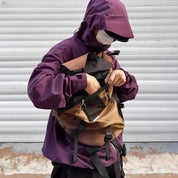 Uomo con giacca viola e mascherina apre zaino marrone e nero. Moda urbana, abbigliamento outdoor, accessori funzionali.