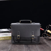 Elegante borsa ventiquattrore in pelle nera con fibbie dorate, ideale per lavoro e ufficio. Design classico su sfondo scuro, perfetta per professionisti.