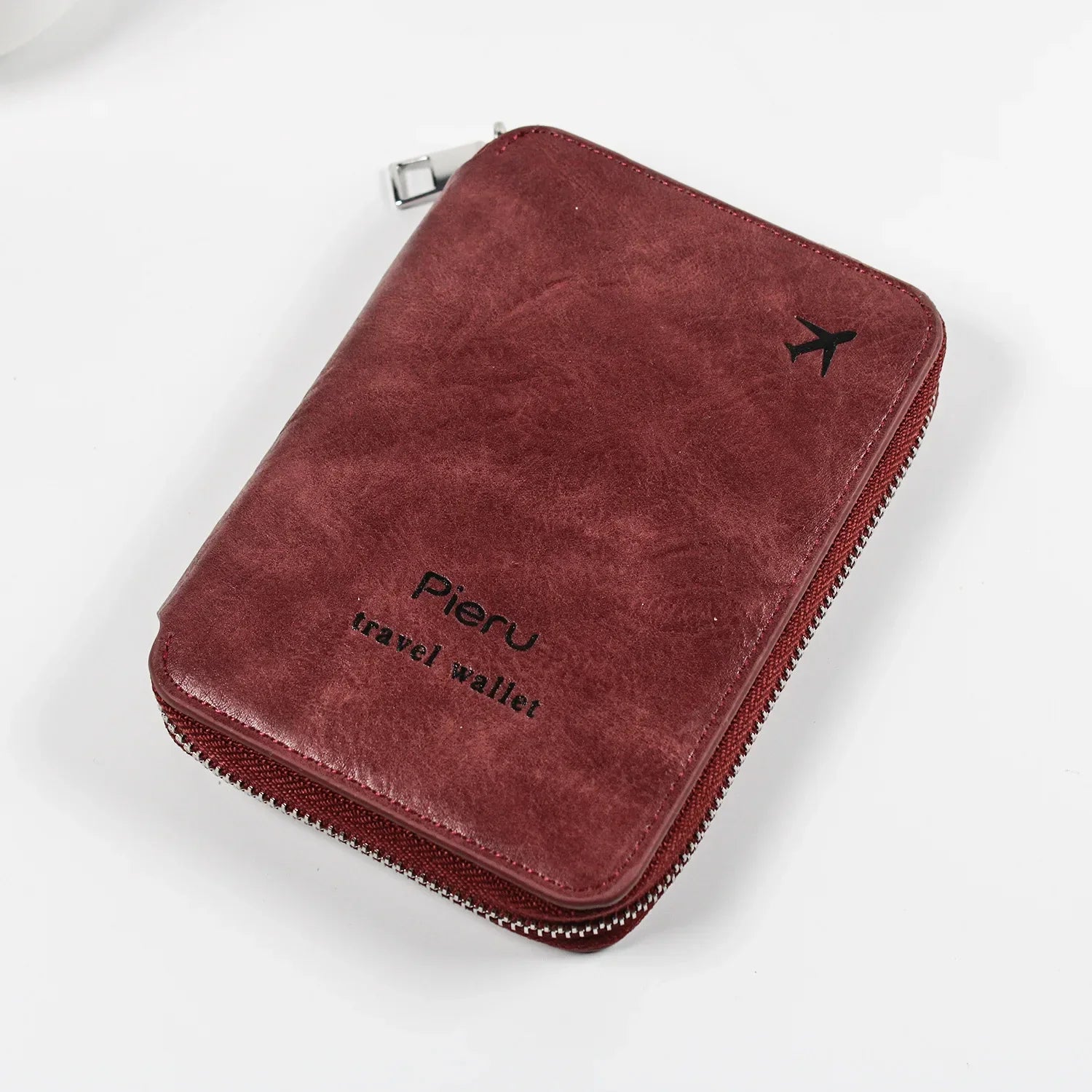 Portafoglio da viaggio in pelle marrone Pieru con cerniera, logo aereo, ideale per documenti e carte. Accessorio elegante e funzionale per viaggiatori.