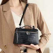 Borsa a tracolla nera in pelle effetto coccodrillo, elegante e moderna, indossata da donna in giacca beige. Accessorio moda femminile di tendenza.