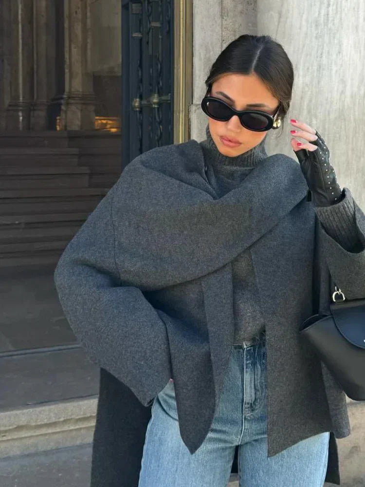 Donna con occhiali da sole, cappotto grigio elegante, guanti in pelle nera e jeans, moda autunnale, stile urbano sofisticato.