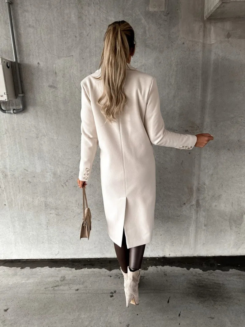 Donna di spalle con cappotto bianco elegante, stivali beige e borsa a mano, su sfondo grigio. Moda autunnale, stile sofisticato.