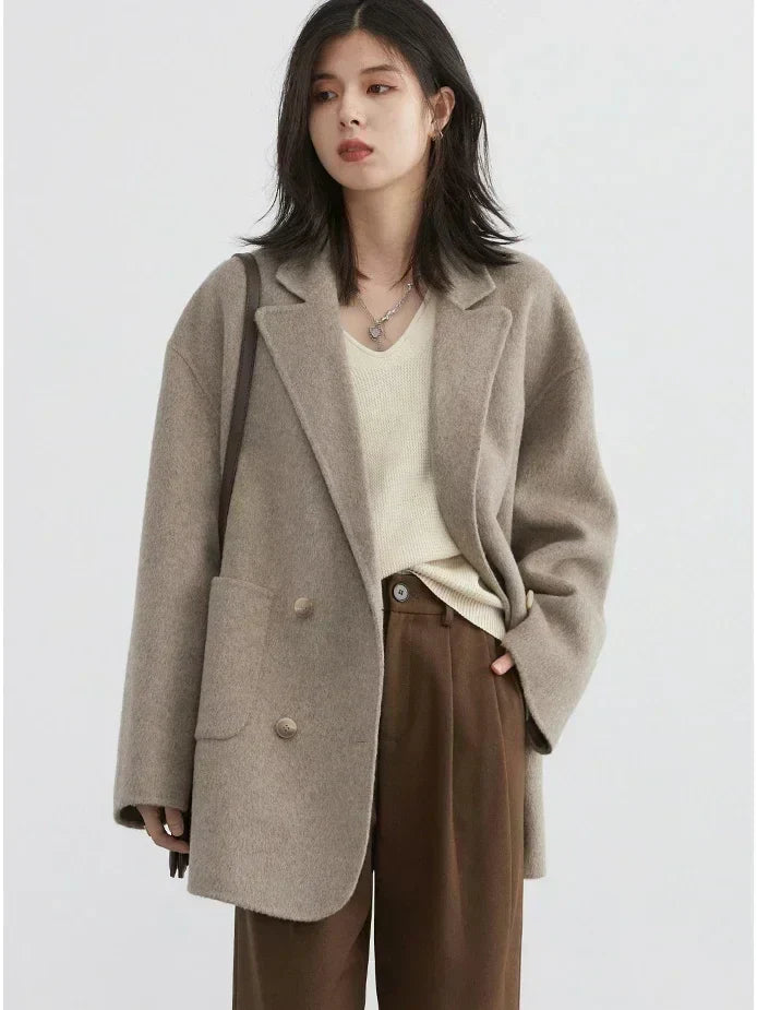 Donna con cappotto oversize beige, maglione crema e pantaloni marroni. Moda autunnale, abbigliamento casual elegante, stile minimalista.