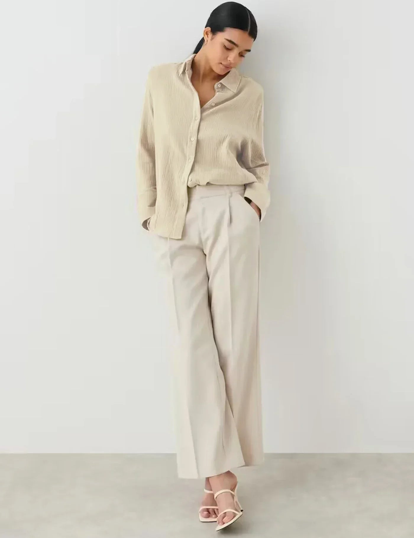 Donna con camicia beige e pantaloni larghi bianchi, posa elegante. Moda femminile minimalista, abbigliamento casual chic, tendenze 2023.