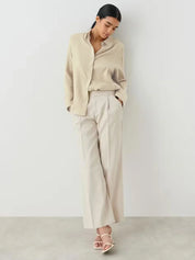 Donna con camicia beige e pantaloni larghi bianchi, posa elegante. Moda femminile minimalista, abbigliamento casual chic, tendenze 2023.