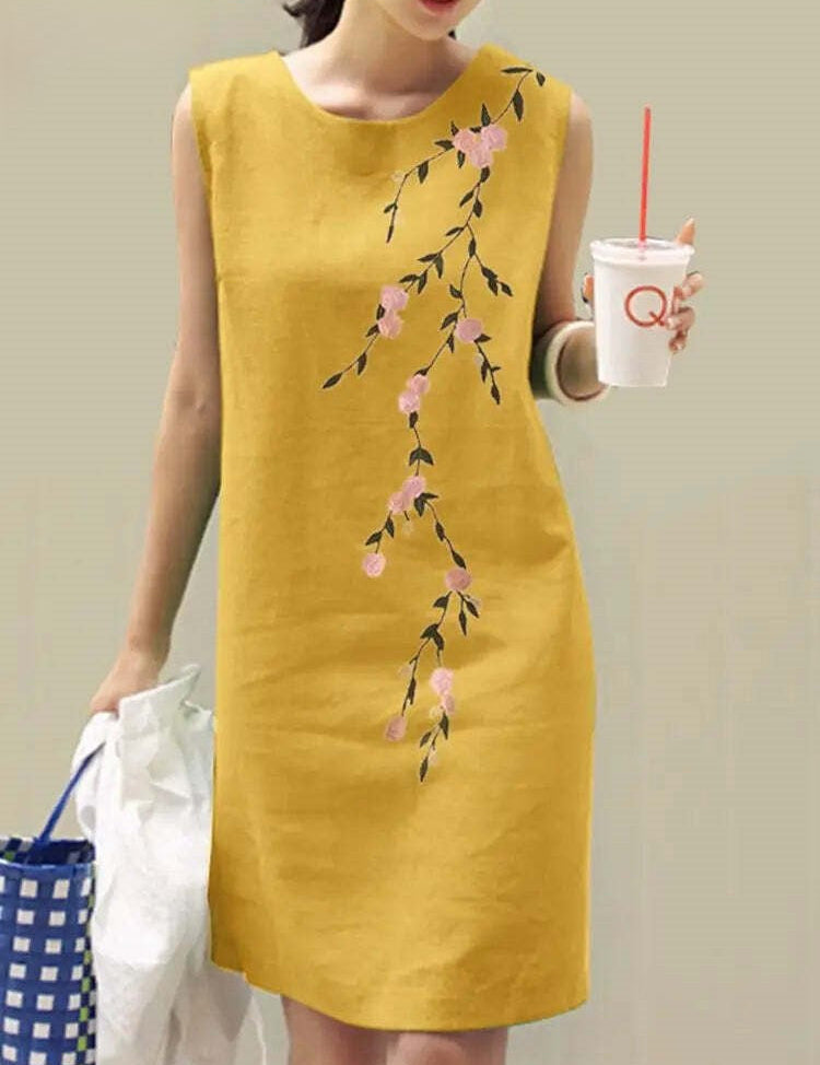 Abito estivo giallo senza maniche con stampa floreale rosa, donna che tiene una bevanda e una borsa a righe blu. Moda casual elegante.