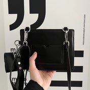 Borsa a tracolla nera in pelle sintetica con tasca frontale, dettagli in metallo argentato e cinturino regolabile. Design moderno ed elegante.