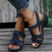 Sandali donna blu con zeppa, decorati con fiori, indossati con jeans strappati e cavigliera dorata. Scarpe estive eleganti e comode.