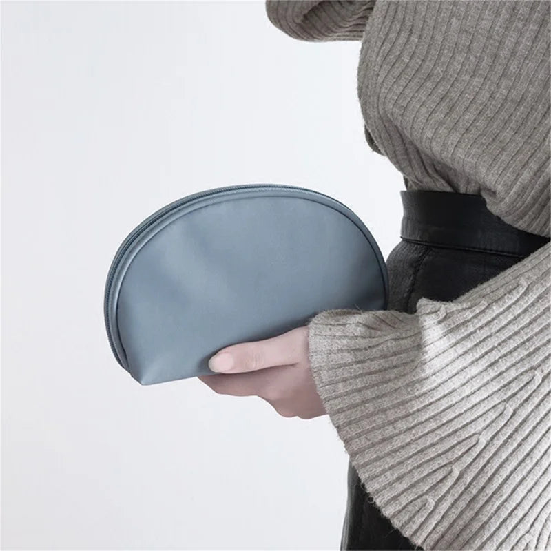 Donna con maglione grigio tiene una pochette blu in mano. Accessorio moda elegante, ideale per cosmetici o piccoli oggetti personali.