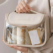 Borsa trasparente da viaggio in PVC beige, con cerniera e manico, contenente flaconi e accessori. Ideale per cosmetici e articoli da toeletta.