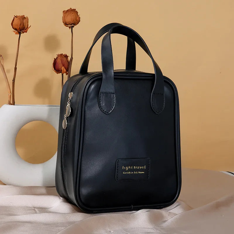 Borsa da viaggio nera in pelle PU con manici, design compatto, chiusura a zip, sfondo beige, decorazione floreale secca. Elegante e pratica.