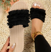 Sandali donna beige con fascia nera in tessuto frangiato, indossati su tappeto intrecciato. Moda estiva, calzature casual eleganti.