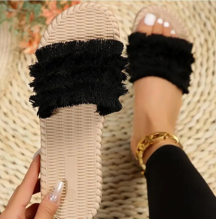 Sandali donna beige con fascia nera in tessuto frangiato, indossati su tappeto intrecciato. Moda estiva, calzature casual eleganti.