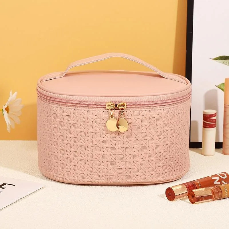 Astuccio cosmetico rosa con motivo intrecciato, chiusura a zip dorata, manico superiore. Accessorio elegante per trucco e bellezza.